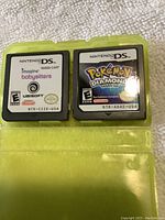 Two Nintendo DS game cartridges placed side by side on a light surface inside a transparent yellow case. One cartridge is Pokémon Diamond Version, the other is Imagine Babysitters by Ubisoft.