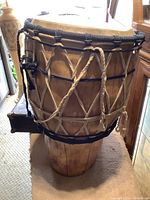 Side view of the African djembe drum showing the carved wooden body, rope tuning system with black and natural rope, and natural skin drumhead.