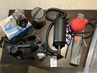 Camping items displayed including air pumps, camping lanterns, headlamp, and fishing reel arranged on floor.