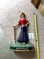 Full front view of the cast iron woman golfer door stop showing size comparison with measuring tape and MaxSold card.