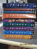 Stack of nine DVD box sets for each season of Friends TV series with distinct color-coded spines and season labels.