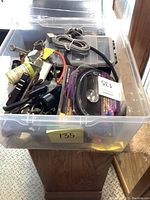 Clear plastic container filled with various hardware, clamps, cables, and a Scosche speaker in packaging visible on top.