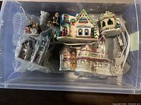 Photo showing the entire container with assorted Christmas village ceramic buildings and figurines, some wrapped in plastic.
