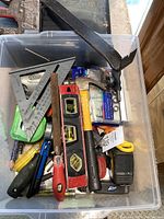 Top-down view of plastic container filled with assorted hand tools including hammers, level, staple gun, screwdrivers, saw, and measuring tapes.