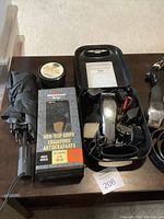 Photo of male personal items on a table including umbrellas, box of non-slip grips, wax tin, and clipper kit in case