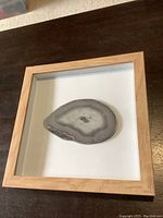 Polished geode slab in wooden shadow box frame on dark table surface.
