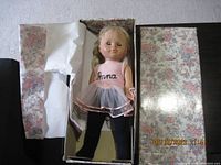 Photo showing vintage Anna Zapf ballerina doll lying in floral box with tissue paper, doll wearing pink ballet dress with 'Anna' embroidered on chest.