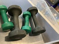 Four dumbbells, two black hexagonal 10 lb and two green round 5 lb, arranged on a metal surface