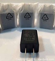 Front view of one USB power adapter block in front of three sealed adapters in plastic bags.