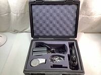 Open black hard case showing interior compartments with Brady label printer parts, spool of label tape, and two AC adapters with cords inside foam cutouts.
