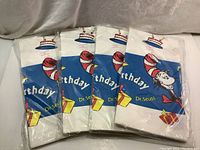Four sealed plastic table covers with colorful Dr. Seuss The Cat In The Hat birthday design featuring cake and presents.