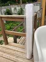 Sealed white fine art paper roll standing upright wrapped in plastic outside on a wooden deck.