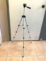 Full length view of the taller lightweight tripod standing on tiled floor, showing adjustable aluminum legs and quick release pan head