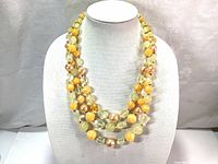 Front view of the three-strand vintage necklace displayed on a white torso bust, showing the variation of yellow, peach, and gold-tone beads.