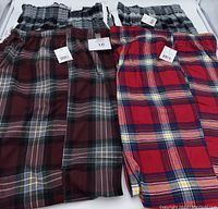 Four pairs of men's George pyjama pants in various plaid patterns and colors laid out side by side showing elastic waistbands and original tags
