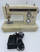 Side view of Kenmore sewing machine showing beige finish, stitch selector panel, dials, and power cord with foot pedal laid in front.