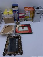 Complete lot of kitchen tools including egg maker, pasta and cookie makers, baby food grinder, sugar canister, candle holder, and picture frames on white surface.