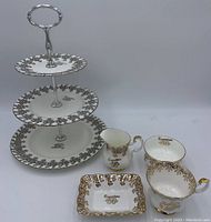 Front and side view of 25th Anniversary 3-tier cake stand with visible intricate dark floral pattern and silver grip handle, shown with 50th Anniversary cream, sugar, cup, and dish items.