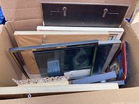 Box packed with various picture frames including black, white, and golden ornate frames