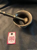 View of metal mortar with pestle inside, showing the interior and overall shape.