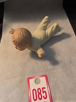 Side view of porcelain baby figurine lying face down with arms extended.
