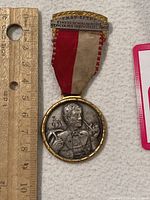 Full view of the medal hanging next to a ruler, showing size and inscriptions on the ribbon and bar.