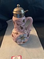 Front view of pink ceramic syrup jug with metal lid and hand painted floral design.