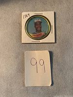 Photo showing one 1989 Topps Fred McGriff baseball coin in a white cardboard holder with handwritten '1989' and the number '99' on paper below.
