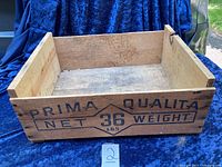Side view of the wooden crate showing 'PRIMA QUALITA NET 36 LBS WEIGHT' printed in black.