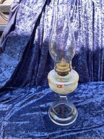 Full view of vintage glass oil lamp with glass chimney on blue fabric background.