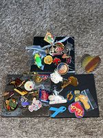 Top view showing the array of over 30 assorted pins and brooches scattered on a black and carpet surface for display.