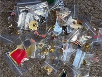Collection of assorted collector pins and brooches in small plastic bags scattered on carpeted surface