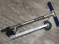 Complete child’s Razor scooter folded with blue foam handle grips and metal base on floor.