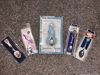 Five souvenir spoons arranged on fabric; each in original packaging featuring historical or regional designs