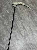 Full view of the scythe showing the black handle and curved skeleton-shaped blade.