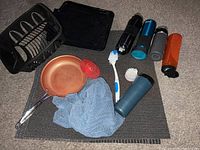 Overview of kitchen items, including copper frying pan, dish rack, water bottles, scrubbing brushes, dishcloth, and mats.
