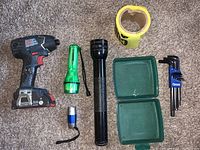 Lot showing all items: power drill, 3 flashlights, Allen wrench set, caution tape, and Tupperware box arranged on carpet.