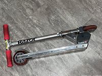 Side view of the silver Razor scooter folded with red grips and wheels.