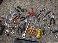 Tools spread out on carpet showing various hand tools including wrenches, pliers, screwdrivers, and scissors.