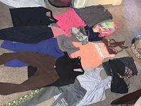 Full lot of women's gym clothes and swimwear laid on carpet, including tops, bottoms, swimwear, multiple colors and patterns represented.