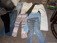 View of nine pairs of women's pants and jeans laid on floor showing variety of styles, colors and sizes between 24 and 28
