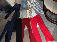 Eight pairs of women's pants laid out on carpet floor showing variety of colors and styles including denim and colorful stretchy pants.
