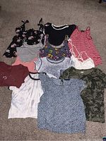 All 11 women's tops laid out on carpet floor, showing various prints and colors