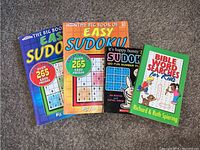 Front view of four puzzle books including three Sudoku books and one Bible Word Search for Kids book.