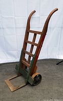 Full front angle view of the antique wooden hand cart with cast iron base, upright handles and wheels showing the structure and condition.
