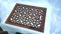 Rectangular cast iron grate with heavy rust and oxidation, displaying a decorative lattice design with intersecting lines and floral details.