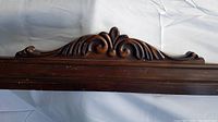 Close-up of carved decorative detail on top center of wood trim piece