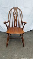 Angled side and front view of the antique wooden armchair highlighting the contoured wooden seat and turned legs.