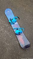 Full view of the Echos youth snowboard with bindings laid on asphalt, showing length and width.