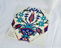 Front view of the square hand-glazed Iznik tile with floral traditional Anatolian motifs in red, blue, turquoise, and green colors, positioned in protective corner holders on a white background.